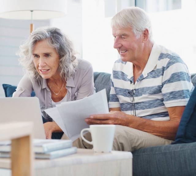 Older Man and Woman holding papers at a computer.